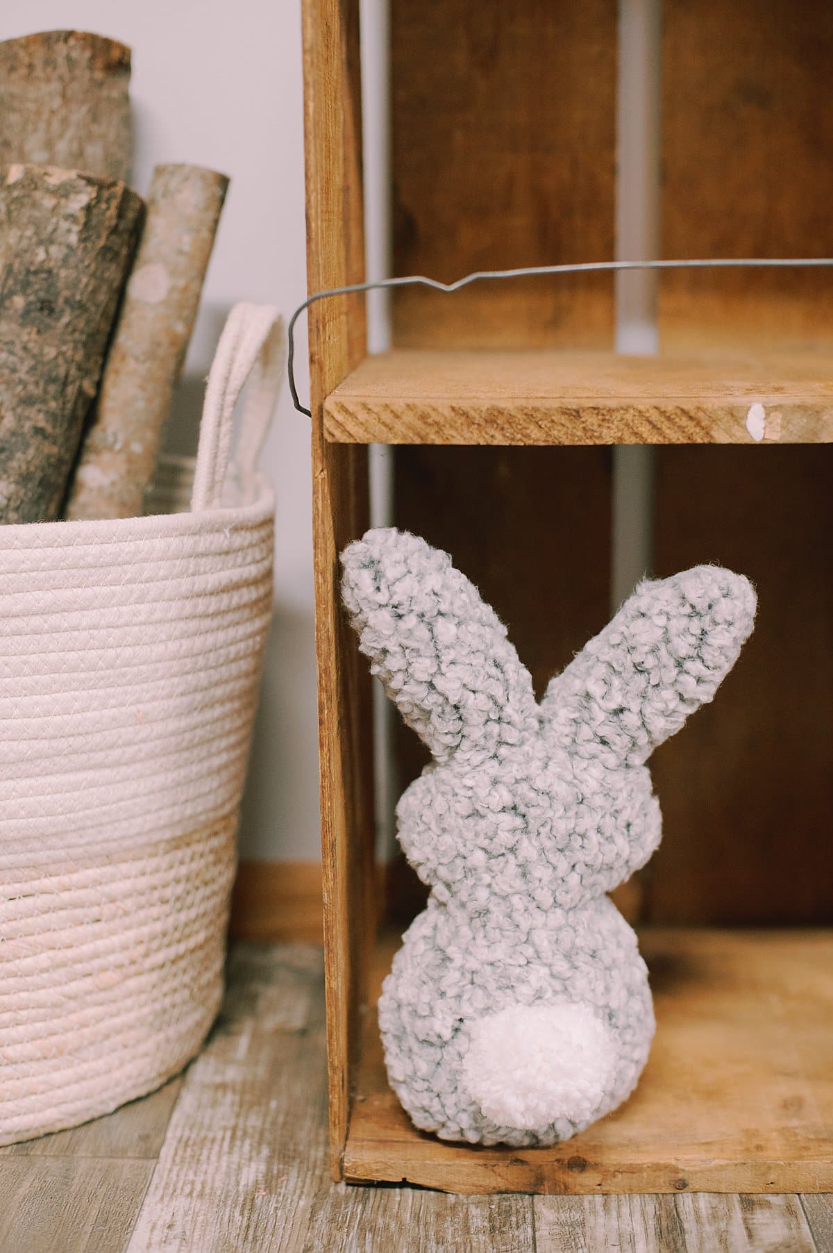 A gray stuffed bunny made with recycled sherpa clothing, and a yarn pom pom sewn on it.