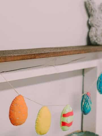 Easter garland made with felt egg shapes in varying colors hanging from wood mantel.