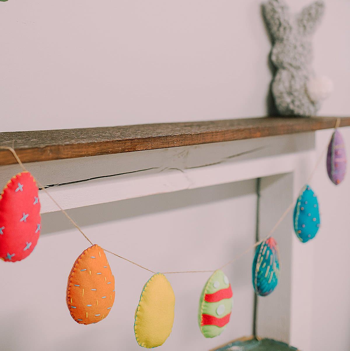 Easter garland made with felt egg shapes in varying colors hanging from wood mantel.