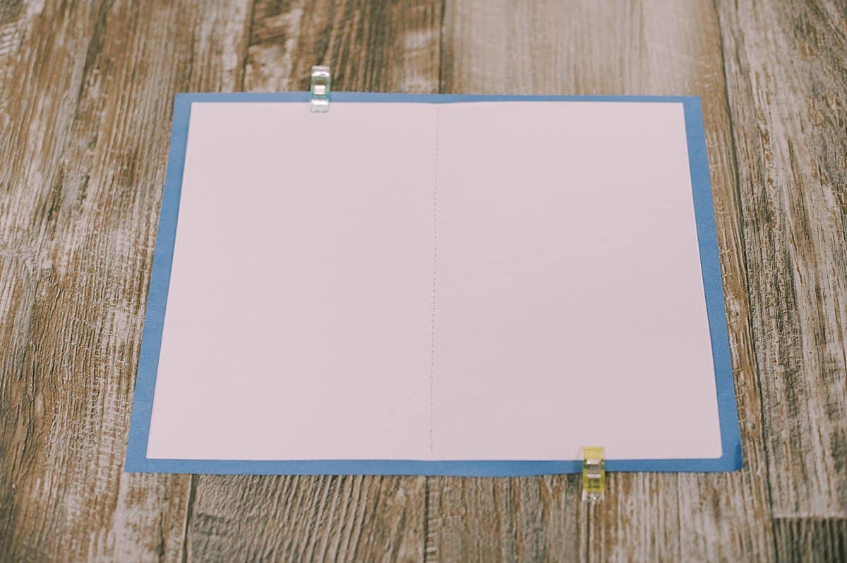 The inside of a handmade book with a blue cover and white interior pages, sewn together with a sewing machine and held together with quilt clips.