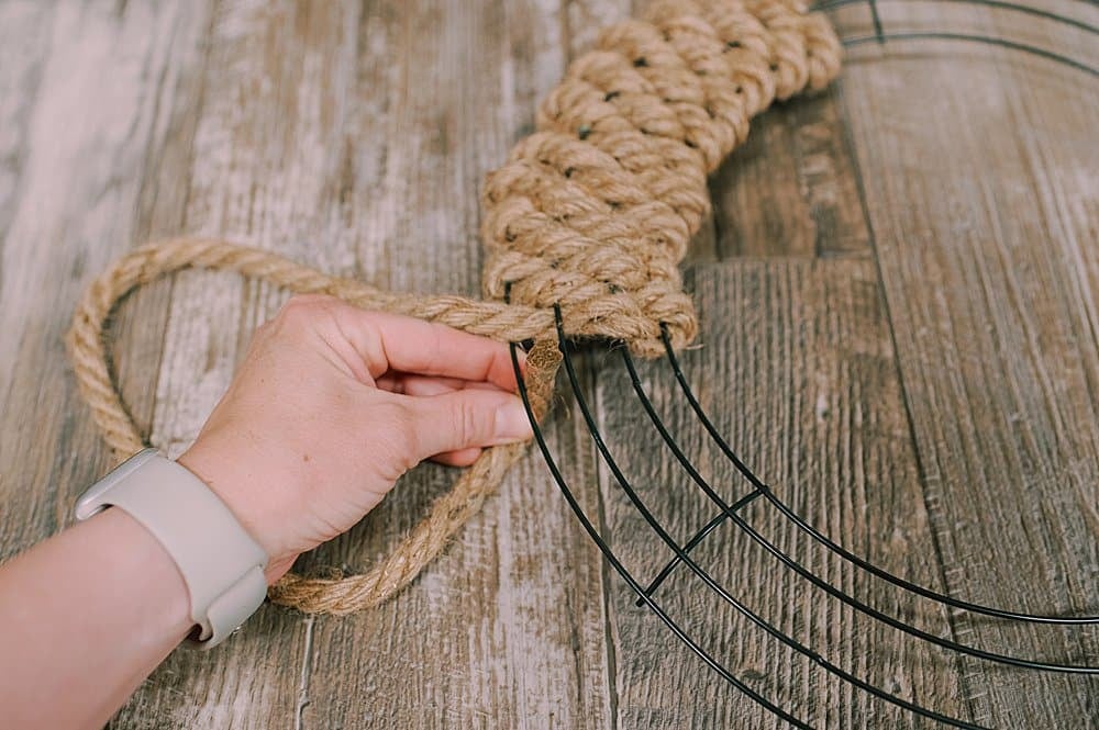 A jute rope being woven through a wire wreath form, coming up from the outer edge.