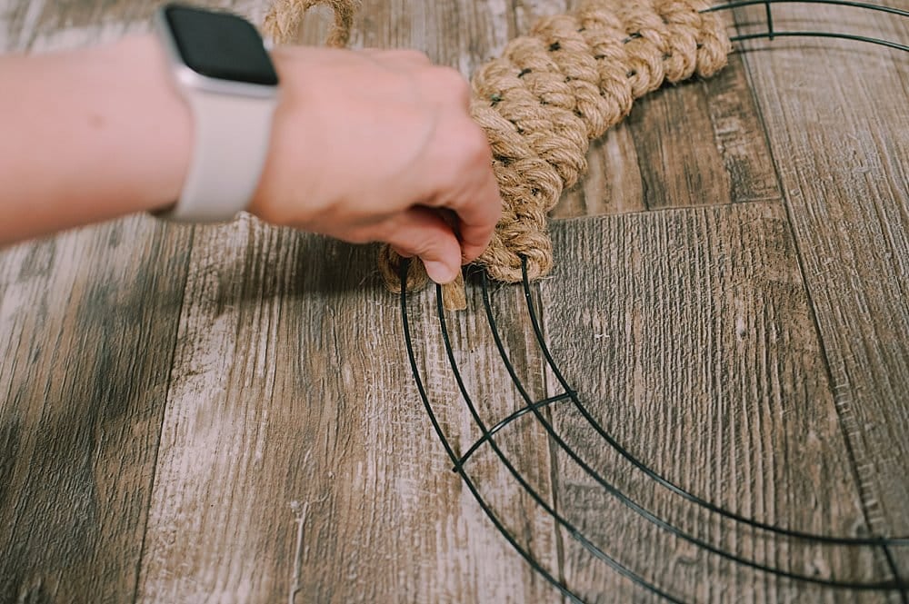 A jute rope being woven through a wire wreath form, going over the next wire.