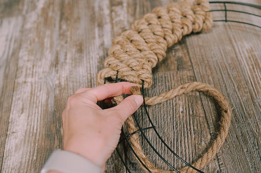 A jute rope being woven through a wire wreath form, coming under the next wire.