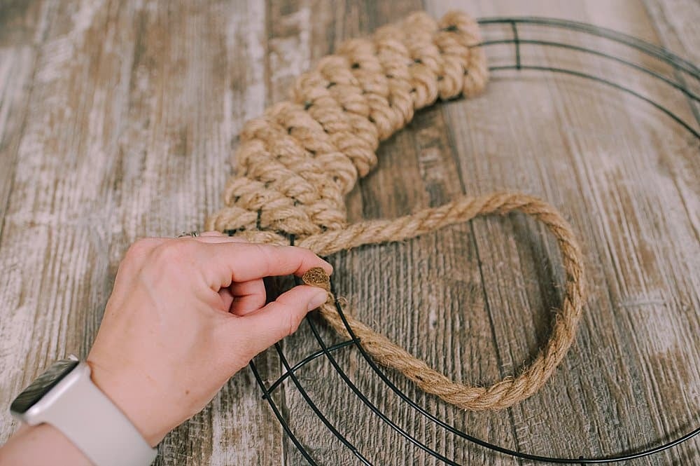 A jute rope being woven through a wire wreath form, coming over the final wire edge.