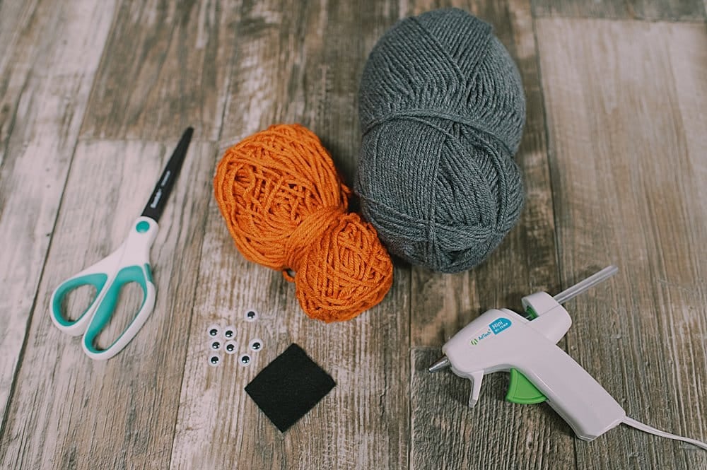 The supplies needed for yarn tassel ghosts, including yarn, scissors, googly eyes, felt, and a hot glue gun.
