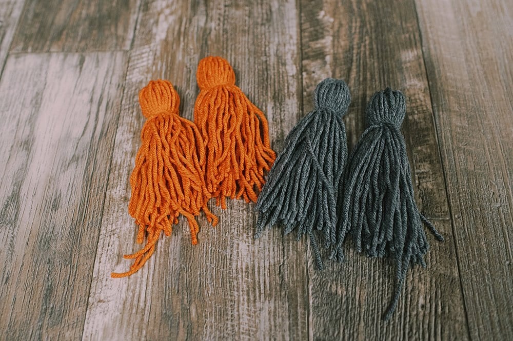 Orange and gray yarn tassels laying on a wood floor.