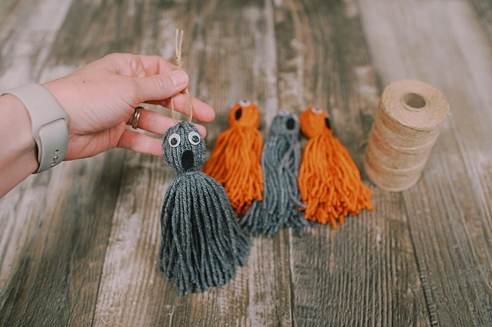A yarn tassel ghost with googly eyes and a felt mouth, with a hanging string on top to make an ornament.