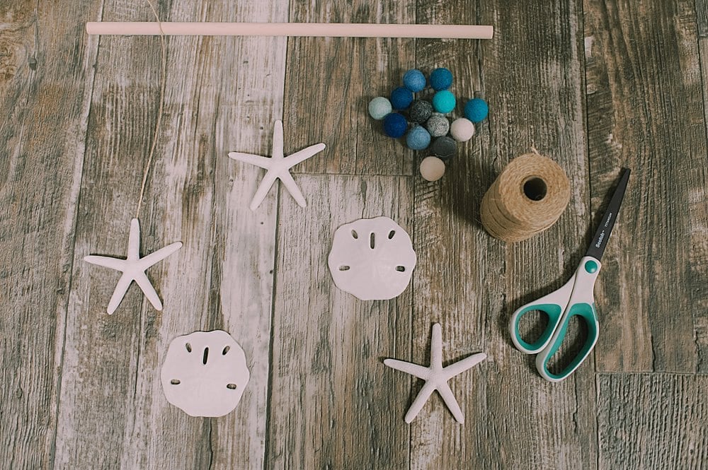 Learn how to make a DIY ocean wall hanging with plastic sand dollars and star fish from the Dollar Tree, plus felt balls and twine!