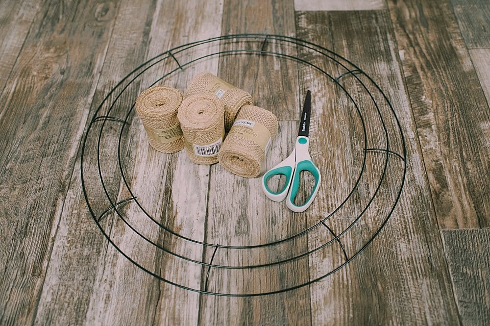 Supplies to make a burlap wreath, including a wire wreath form, rolls of burlap ribbon, and scissors.