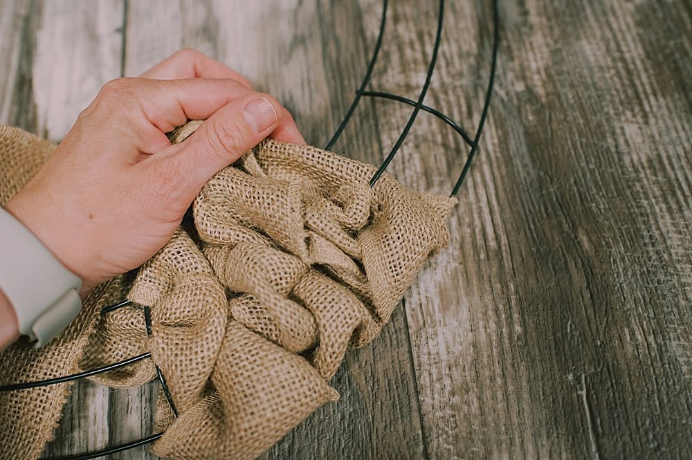 A hand moving burlap ribbon around on a wire wreath form.
