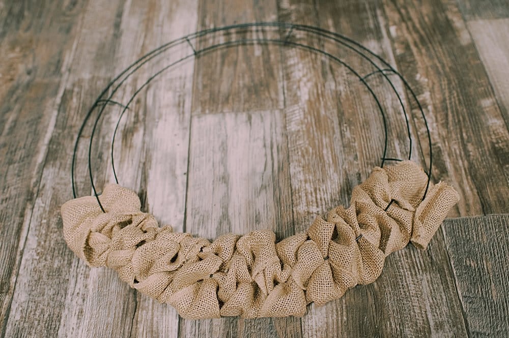 Burlap ribbon halfway wrapped around a wire wreath frame in the process of making a wreath.
