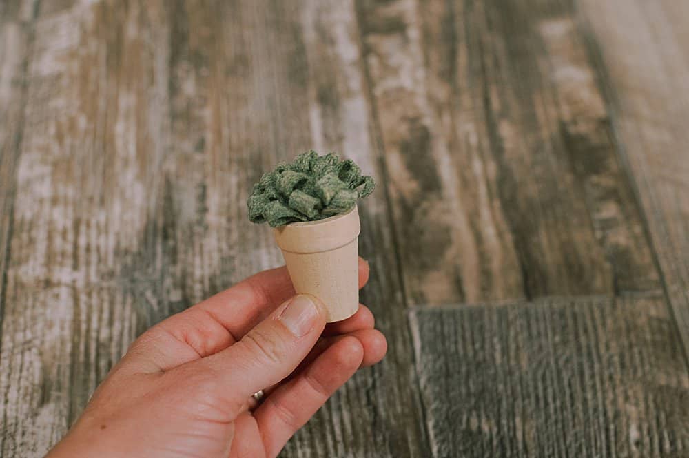 Green felt plant inside small wood pot, help in a hand.