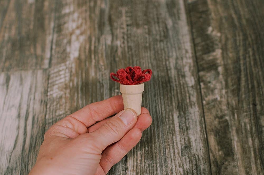 Red mum made out of felt, inside a thimble-sized wood pot.