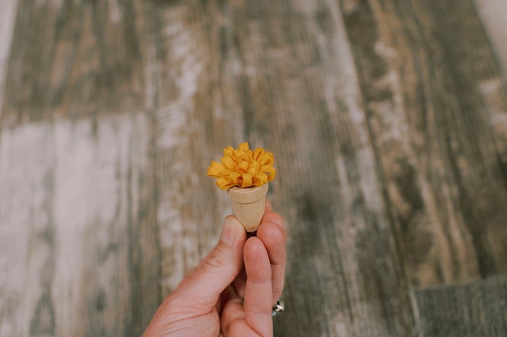 Yellow fluffy felt flower inside small wooden pot.