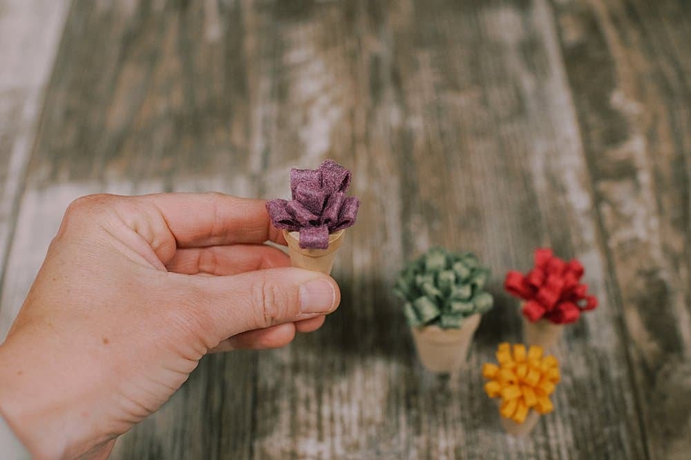 A tiny wooden pot with a felt flower inside it being held up by a hand.