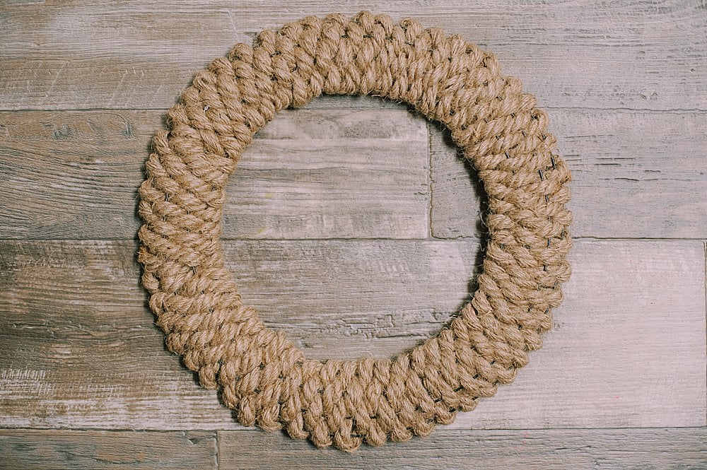 A wreath made out of rope woven into a wire wreath form laying on a wooden surface.