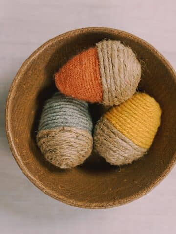 A wooden bowl with plaster easter eggs in it. The plastic eggs are wrapped in yarn and twine to look like DIY acorns.