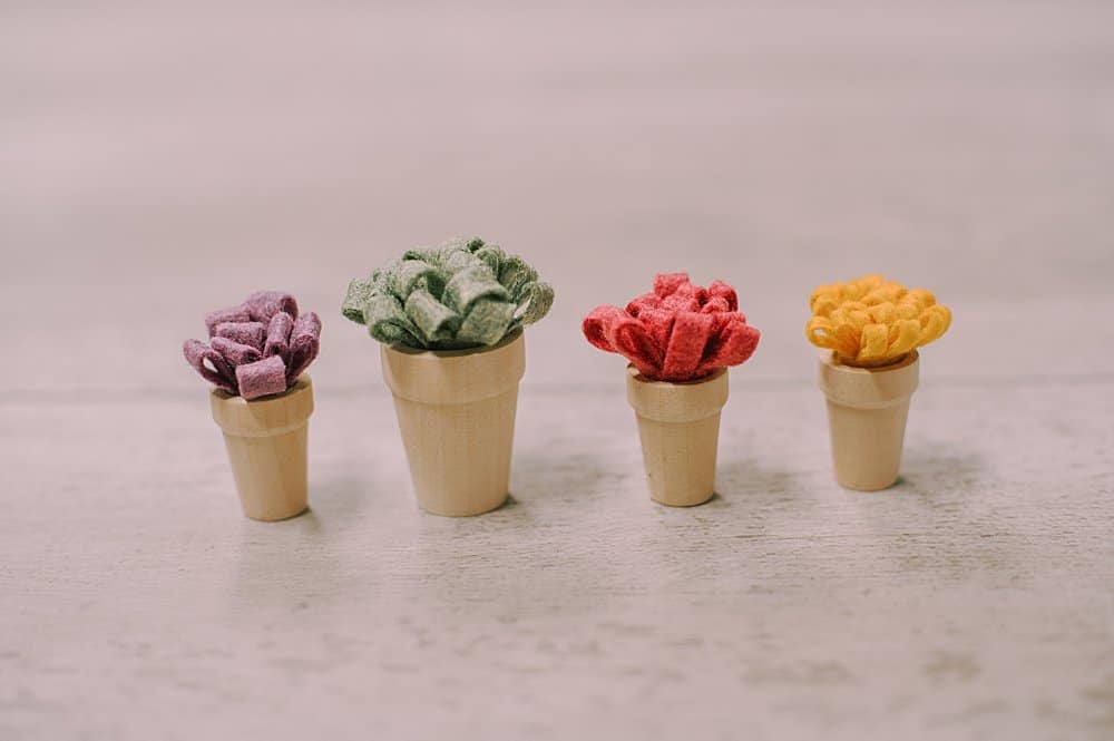 Four little wooden pots with felt flowers inside them.