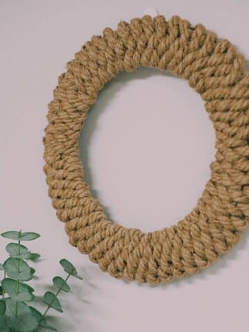 Photo showing a wreath made out of jute rope hanging on a wall above a shelf with a plant on it.