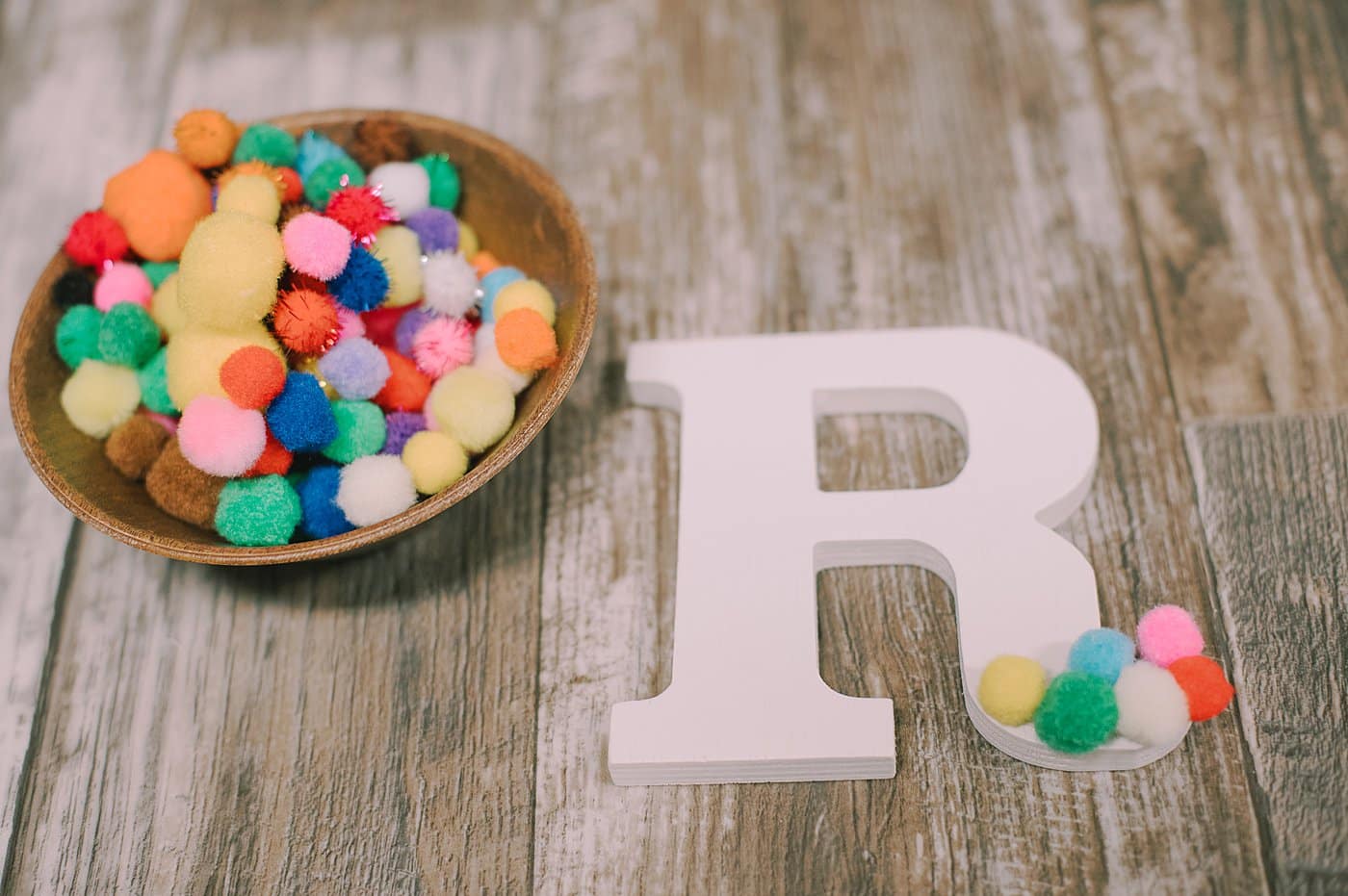 Hot glue pom poms onto a wooden letter.