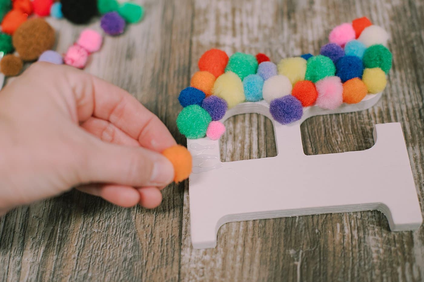 Hot glue pom-poms onto a wooden letter.