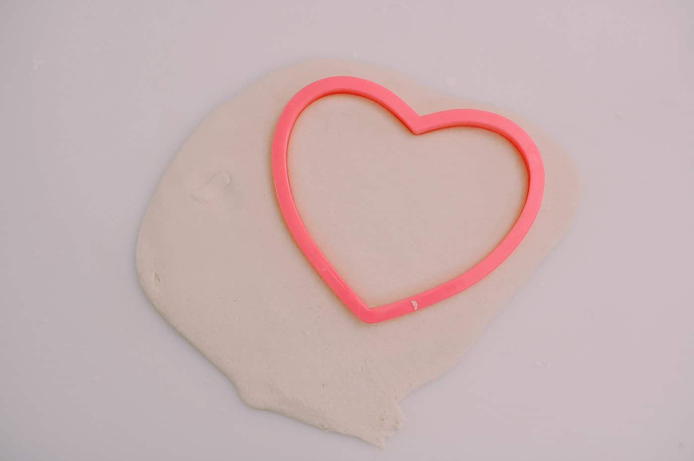 A cookie cutter, cutting out a heart shape from salt dough.