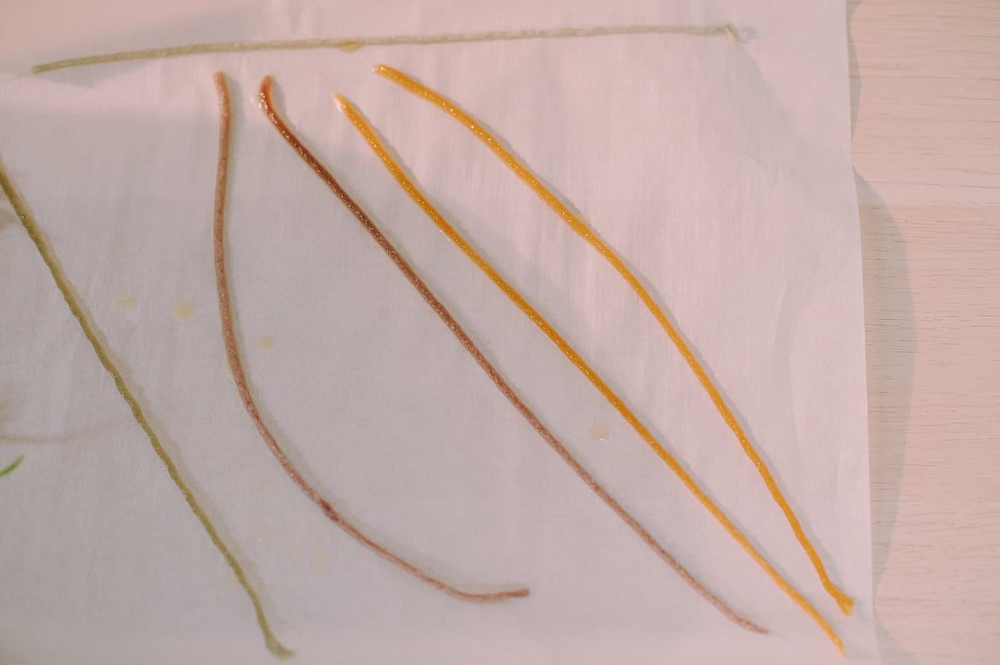 Pieces of yarn that are dipped in beeswax, laying on parchment paper to cool and harden.