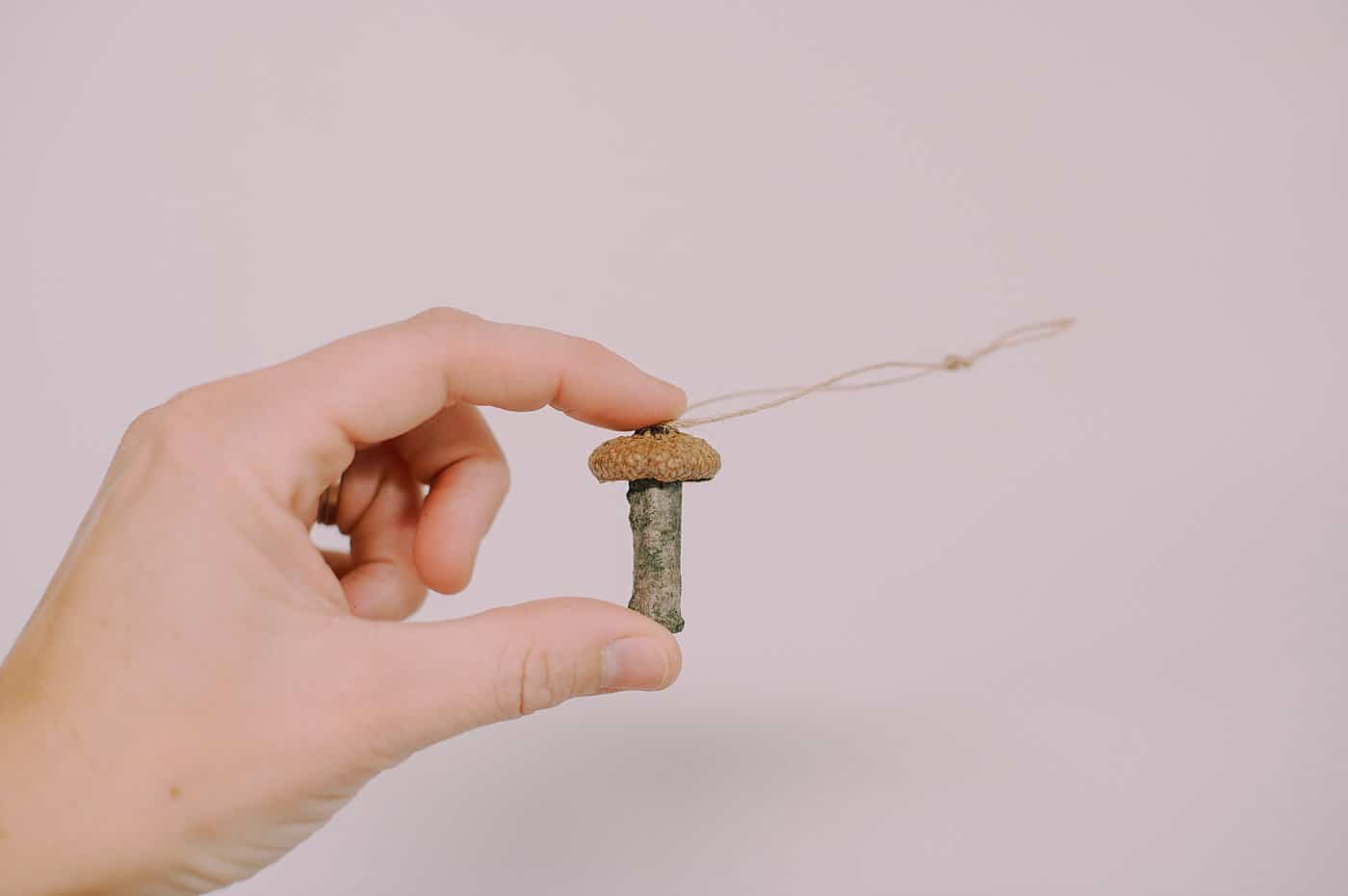 An acorn cap mushroom ornament with a stick stem and a twine hanging string.