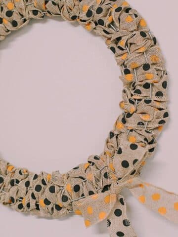 A Halloween wreath made with burlap ribbon with black and orange polka dots on it.