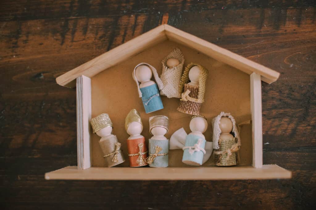 A wooden nativity stable and handmade nativity set made with wooden peg dolls and fabric scraps for clothes.