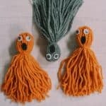 Yarn tassel ghosts made with orange and gray yarn, googly eyes, and black felt for the open mouth.