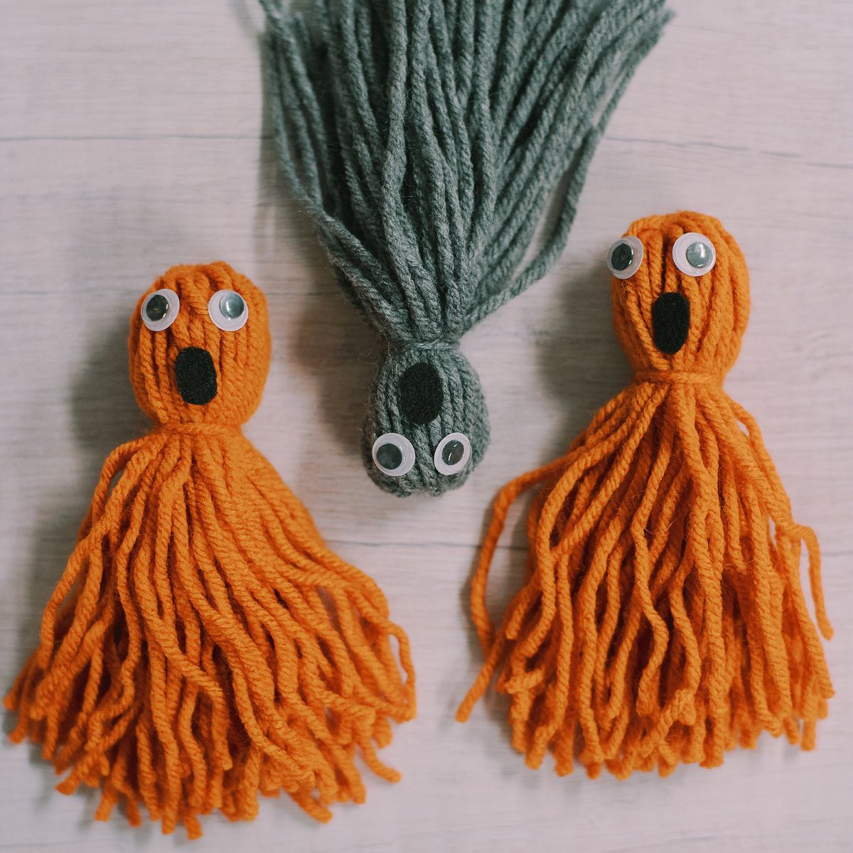 Yarn tassel ghosts made with orange and gray yarn, googly eyes, and black felt for the open mouth.
