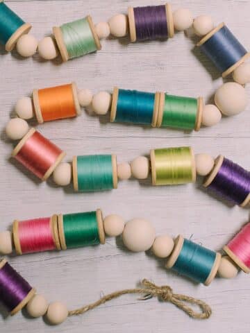 Colorful spools of thread and wooden beads threaded on twine to make a garland.