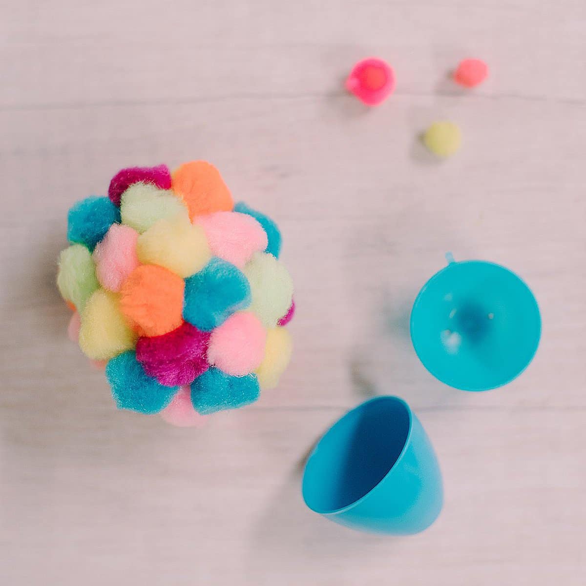 A plastic Easter egg with craft store pom poms hot glued to the outside to make a pom-pom covered Easter egg.