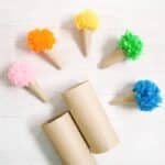 Cardboard ice cream cones made out of toilet paper tubes with colorful yarn pom poms on top.