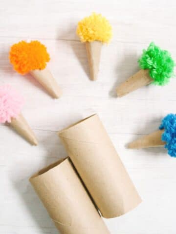 Cardboard ice cream cones made out of toilet paper tubes with colorful yarn pom poms on top.