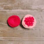 Two types of felt rose flowers laying on a wooden surface.