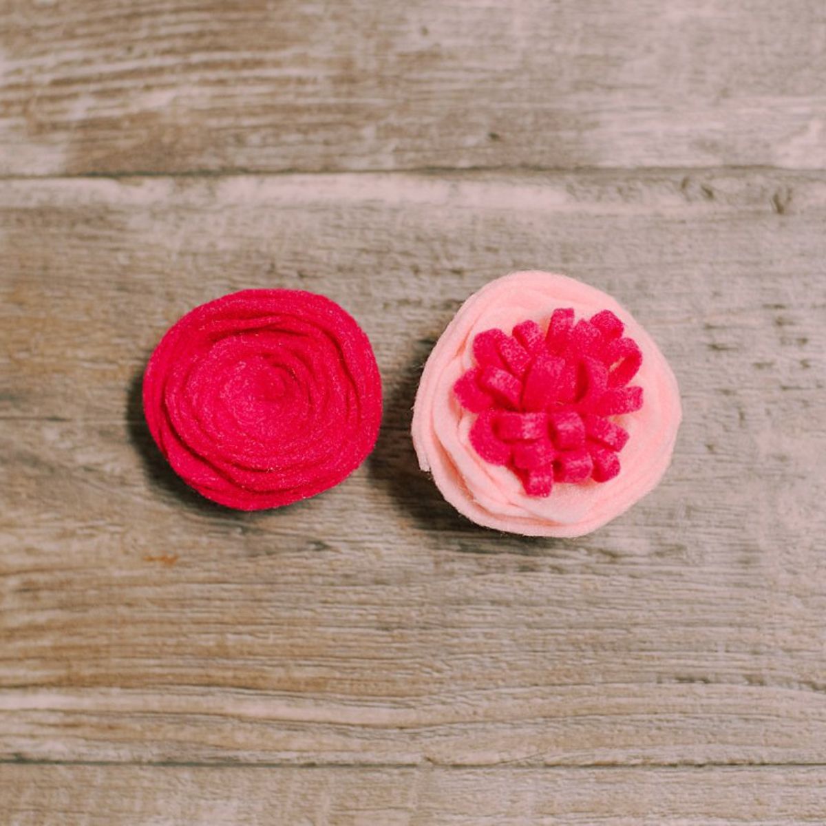 Two types of felt rose flowers sitting side by side on a wood surface.