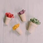 Felt mum flowers in tiny wood pots laying on a white wood surface.