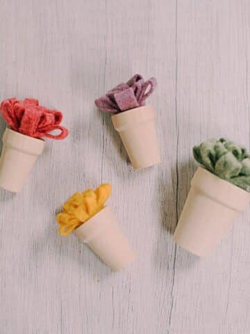 Felt mum flowers in tiny wood pots laying on a white wood surface.