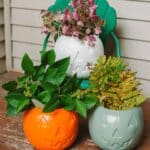 Painted plastic pumpkin treat buckets with jack-o-lantern faces, filled with plant clippings to serve as front porch decor.