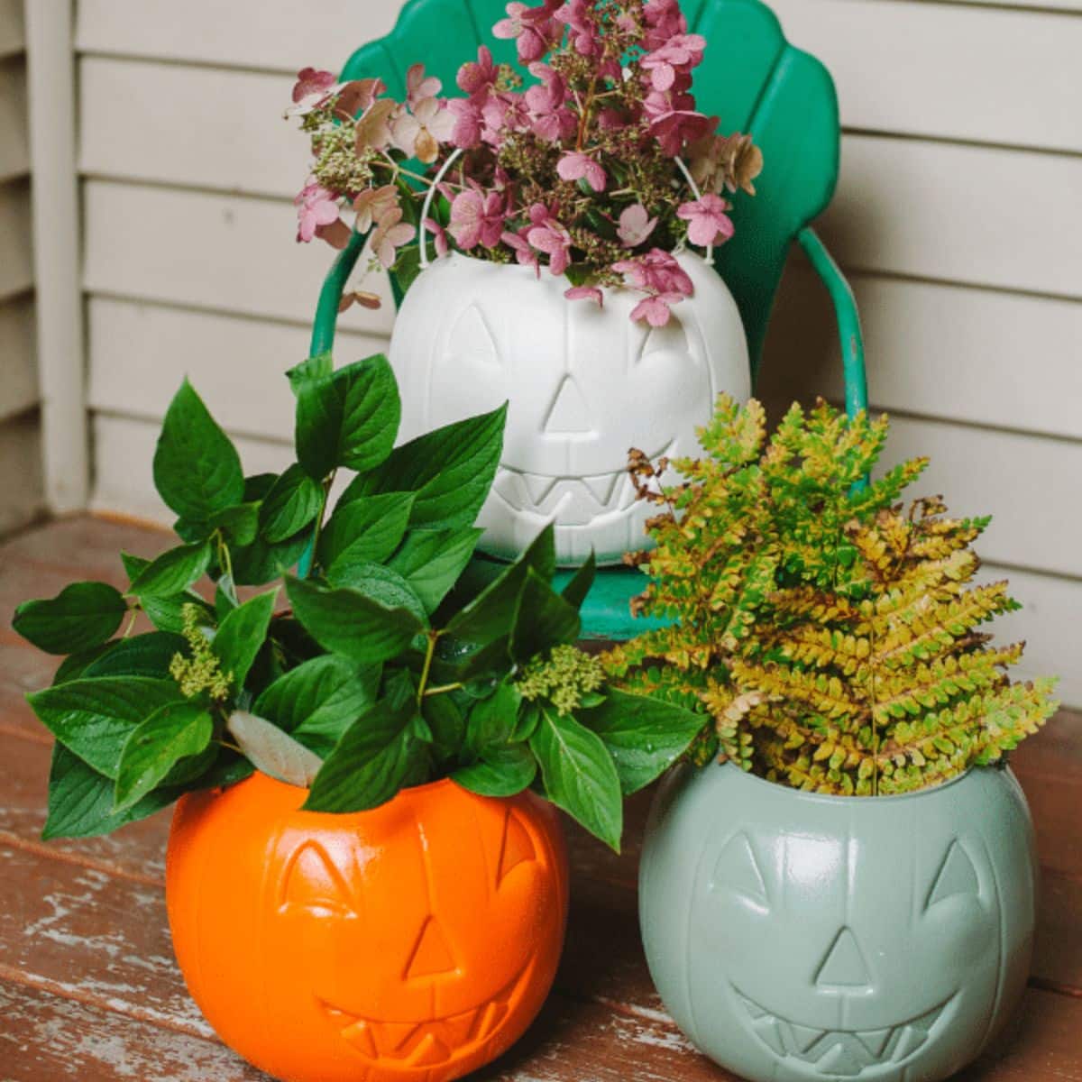 Plastic pumpkin treat buckets spray painted orange, green, and white, and used to hold flower and fern clippings on a front porch.